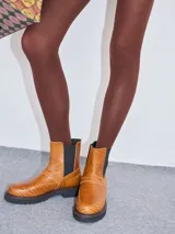 Bota corta color cuero con textura de piel de cocodrilo, con elásticos laterales negros y suela de goma negra con pespuntes en color crudo.