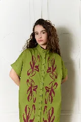 Vestido largo verde militar de popelina de algodón, con diseño oversized, cuello mao, mangas cortas, bolsillos laterales y cierre frontal con botones. Presenta un estampado de flores grandes en la parte superior y franjas horizontales de colores en el ruedo.