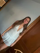 Vestido corto negro con escote en V profundo, estilo halter con tiras para atar al cuello. Presenta un diseño ajustado en el busto con tiras ajustables bajo el mismo que se cruzan y anudan en la espalda, y falda con volado en el ruedo con detalle de encaje.