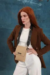 Phonebag pequeña color mostaza, confeccionada en cuero sintético, con solapa frontal y correa ajustable con logo de la marca.