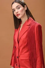 Blazer rojo de corte estructurado con solapas clásicas y cierre de doble botonadura en contraste negro. Presenta flecos largos aplicados en hombros y mangas que aportan movimiento a la prenda.