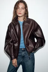 Cazadora estilo bomber de efecto piel en color bordó, con cuello solapa, manga larga, bolsillos delanteros de vivo con botón a presión y bajo elástico. Cierre frontal con cremallera oculta y botones a presión.