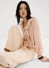 Blusa de seda color rosa pálido con volados frontales, cuello redondo y mangas largas con puños elásticos.