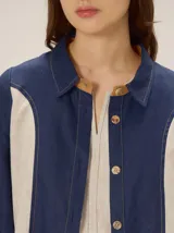 Camisa de lino color blanco con detalles combinados en tonos beige, cuello camisero, cierre frontal con botones oscuros y mangas largas con puños en contraste.