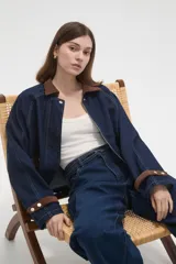 Campera de jean azul oscuro con cuello y puños de pana en color marrón. Presenta cierre frontal, costuras a la vista y detalles de botones metálicos en los puños.