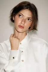 Camisa de satén color blanco, de corte clásico con cuello solapa, manga larga con puños y cierre frontal con botones dorados.