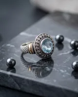 Anillo de plata y oro con circonia central redonda en tono aguamarina, rodeada de detalles texturizados.