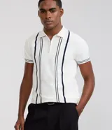 Camisa polo slim de punto, color blanco con rayas verticales oscuras en contraste en el frente y líneas en los bordes de las mangas cortas. Cuenta con cuello polo y cierre frontal parcial con cremallera.