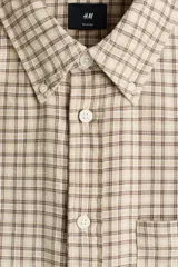 Camisa de sarga de algodón con estampado a cuadros en tonos beige y marrón, cuello americano, cierre frontal de botones, un bolsillo de parche en el pecho y mangas largas.