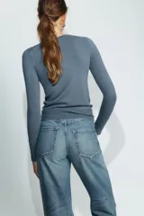 Jersey de punto liso color negro, con cuello redondo y manga larga. Presenta una hilera de cuatro botones dorados decorativos en el puño de cada manga.