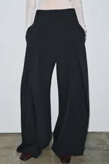Pantalón de tiro medio color negro con raya diplomática, con pinzas delanteras, bolsillos laterales ocultos y pierna ancha. Cierre frontal con cremallera, botón y ganchos metálicos.