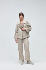 Sacón de diseño amplio con técnica patchwork, confeccionado con retazos de telas de diversas texturas en tonos beige y gris. Presenta mangas ranglan, cuello con solapas y cierre frontal con un único botón.