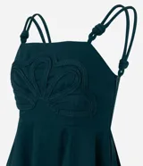 Blusa verde oscuro de viscolino con tirantes dobles ajustables mediante nudos. Presenta un corpiño estructurado con un detalle de flor en relieve en la parte delantera y smock en la espalda para un mejor ajuste. La prenda tiene un bajo peplum.