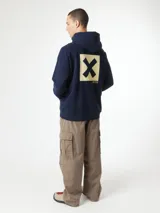 Hoodie azul marino con capucha, bolsillo tipo canguro y gran estampado cuadrado en la espalda con una letra X negra sobre fondo beige.