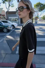 Top de tejido negro con cuello polo y bordes de manga cortos con diseño de ondas en blanco y negro. Tiene un cierre frontal de botones.