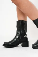 Bota biker de caña media color negro, con hebilla en la parte superior y detalle de aro y tachas en la parte inferior.