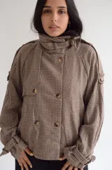 Chaqueta de corte estructurado con estampado cuadrille en tonos marrones y beige. Presenta cuello alto con tira ajustable, cierre frontal con botones, charreteras en los hombros y puños con detalle de hebilla.