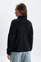 Buzo de polar negro con cuello alto y cierre frontal parcial. Presenta un diseño de corte holgado con mangas largas y costuras horizontales en el pecho.
