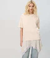 Remera oversized de algodón color beige, de manga corta y cuello redondo, con superposición inferior liviana, bajo asimétrico y aplicación de encaje.