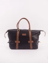 Bolso de viaje tipo tote de gran capacidad, confeccionado en cuero natural negro con detalles en cuero color suela. Presenta doble asa superior, cierre principal con cremallera y correas decorativas verticales con remaches metálicos. Incluye bolsillo interior con cierre, compartimento para celular y forro interno.