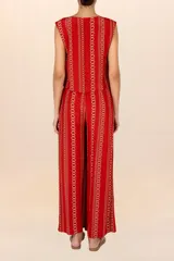 Chaleco sin mangas de color rojo con estampado de cadenas doradas en disposición vertical. Presenta escote redondo y cierre frontal mediante cordones entrelazados.
