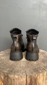 Bota acordonada de cuero con efecto desgastado, suela track de goma negra y costuras a la vista.