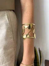 Brazalete dorado con diseño de hojas y estructura abierta.