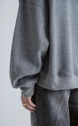 Buzo de cuello redondo con diseño oversize y corte crop. Confeccionado en frisa de algodón color gris melange, presenta un recorte asimétrico en color negro en microfibra con un bolsillo frontal funcional con cierre a presión.