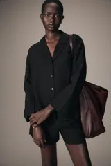 Camisa de estilo pijamero confeccionada en lino 100%, con cuello solapa de muescas, manga larga y cierre frontal con botones. Presenta un diseño de corte recto con bajo asimétrico.