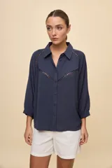 Camisa negra de calce relajado, con mangas 3/4, cuello clásico y cierre frontal con botones. Presenta detalles calados en la parte superior.
