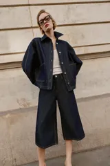 Bermuda de tiro alto confeccionada en denim azul oscuro, con diseño de pernera ancha, cinco bolsillos y cierre frontal con cremallera y botón.