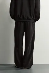 Pantalón jogger de corte relajado en color negro, confeccionado en tejido con elasticidad. Presenta cintura elástica con cordón ajustable y bolsillos laterales decorados con tachas metálicas.