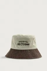 Sombrero bucket confeccionado en tejido de algodón con efecto lavado, diseño bicolor en tonos beige claro y marrón oscuro. Presenta ala ancha con pespuntes y un bordado frontal en contraste.