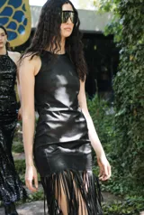 Vestido corto de cuero negro, sin mangas, con cuello redondo y diseño ajustado que presenta flecos largos en el dobladillo inferior.