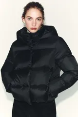 Plumífero corto acolchado color negro, resistente al agua y al viento. Cuenta con cuello subido, capucha extraíble, cierre frontal con cremallera y botones magnéticos, mangas largas con puños elásticos y bajo ajustable con stoppers.