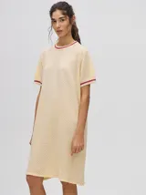 Vestido corto color amarillo claro, tipo remerón, de corte suelto con cuello redondo y mangas cortas. Presenta detalles de líneas en tono bordó en el cuello y en los puños.