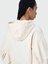 Canguro color crema con capucha, cierre frontal con cremallera dorada, mangas abullonadas 3/4 y logo de la marca en el pecho.