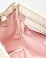 Cartera mediana color crudo de simil cuero, con doble asa de mano, correa ajustable y desmontable, bolsillo frontal con botón a presión, detalles de herrajes plateados y dije colgante en forma de corazón. Cuenta con el logotipo de la marca grabado en la parte frontal.