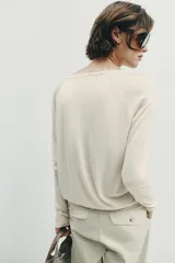 Pantalón de tiro medio con pinzas delanteras, bolsillos frontales y falsos bolsillos con solapa en la parte posterior. Presenta un diseño de pernera holgada que se estrecha hacia el tobillo, con cierre frontal de cremallera y botón.