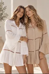 Vestido corto blanco tipo túnica, con mangas largas acampanadas y detalles de bandas con recortes circulares en el pecho y las mangas.