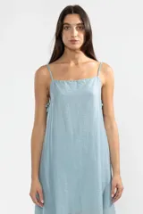 Vestido largo hasta el tobillo color celeste, de tejido arrugado liviano, con escote recto y breteles finos. Presenta lazos en los costados, forro hasta arriba de las rodillas y caída posterior más larga.