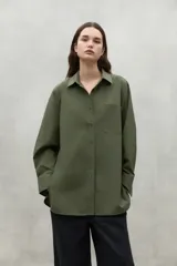 Camisa de manga larga color verde oliva, con cuello clásico, botones frontales y un bolsillo de parche en el pecho. Presenta un corte holgado.