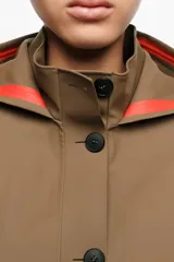 Gabardina marrón de largo medio y corte en línea A, confeccionada en tejido técnico impermeable con exterior de poliéster y poliuretano. Presenta cierre frontal de botonadura simple, cuello alto con capucha ajustable, bolsillos laterales de vivo y mangas largas con trabillas en los puños.