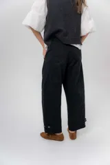 Pantalón de gabardina de algodón color negro, con calce barrel, cintura media baja, recortes de diseño y detalle de botones en el ruedo para ajustar el volumen.