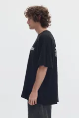Remera boxy negra de algodón, con cuello redondo, manga corta y estampa frontal blanca con texto.