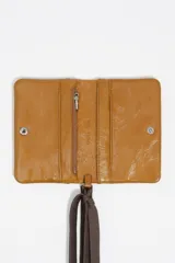 Billetera compacta de cuero color marrón con acabado brillante, cierre de solapa y cordón ajustable de tela marrón con terminales metálicos. Incluye el logo de la marca grabado en la parte frontal.