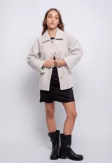 Tapado corto color beige de paño, con cuello clásico, cierre frontal con botones veteados y bolsillos delanteros.