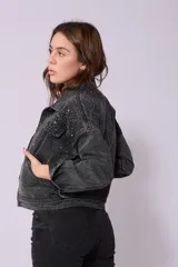 Campera de jean de lavado celeste claro, con diseño clásico de cuello y botones metálicos. Presenta detalles de pequeños brillos o tachas plateadas sobre la tela, especialmente visibles en los bordes de los bolsillos y costuras.