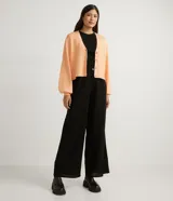 Chaqueta corta de punto color negro, con escote en V, manga larga abullonada, sisa desplazada, abotonado frontal total con botones forrados y puños acanalados.