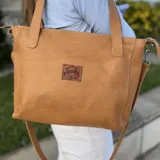 Cartera tipo tote de cuero natural color camel, con textura granulada. Cuenta con doble asa fija para llevar al hombro, correa larga ajustable y removible, cierre superior y bolsillo externo con cierre en la parte trasera.